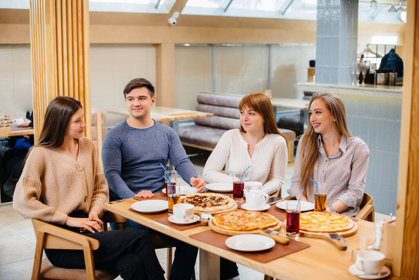 A group of young cheerful friends is sitting in a cafe talking and eating pizza. Lunch at the pizzeria. - Fotoğraf, Görsel