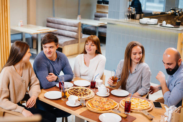 A group of young cheerful friends is sitting in a cafe talking and eating pizza. Lunch at the pizzeria. - Foto, Imagem