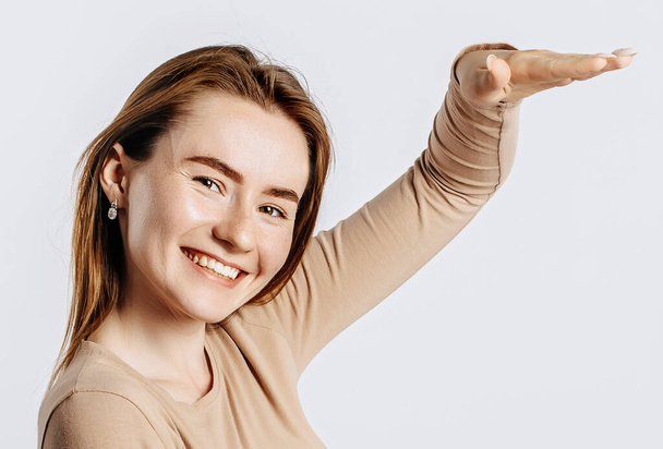 Young beautiful brunette girl smiles and shows big size measure with her hand gesture on a white isolated background - Zdjęcie, obraz