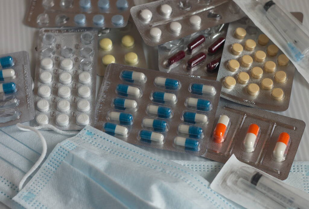Auf dem Tisch liegt eine medizinische Maske und verschiedene Farben und Formen von Pillen und Kapseln in einer Verpackung - Foto, Bild