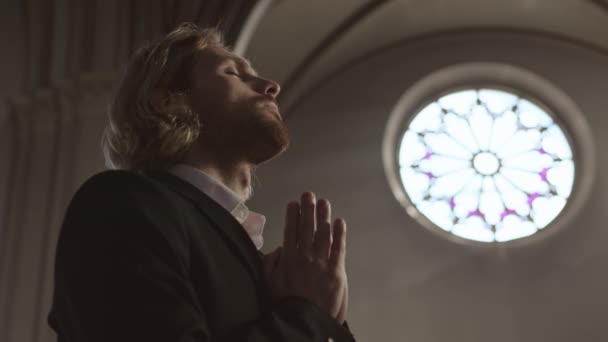 Alacsony látószögű kilátás fiatal fehér hajú férfi zakóban és fehér ingben áll a keresztény templomban, keresztbe magát, majd elmegy - Felvétel, videó
