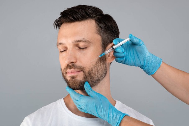 Attractive middle-aged man getting anti-aging procedure, grey background - Photo, Image