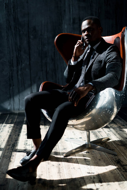 African American director of the company sits in a chair in a suit and talks on the phone - Photo, image