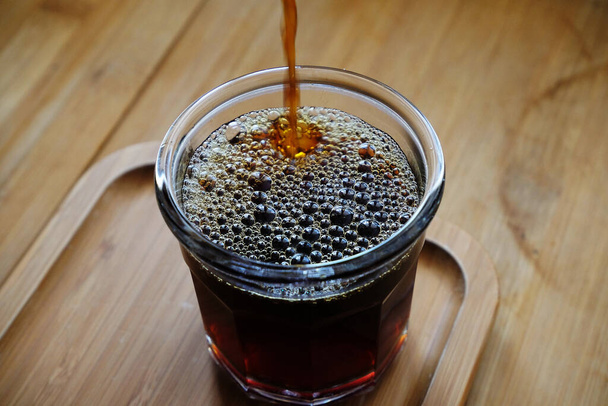 Verter café de filtro negro recién hecho en una taza de vidrio, de cerca. Mesa de madera - Foto, imagen