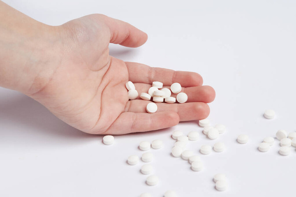 Hrst bílých kulatých pilulek v dětské dlani na bílém pozadí. Ruka držící hromádku malých kulatých léků. Zdravotní a medicínský koncept - Fotografie, Obrázek