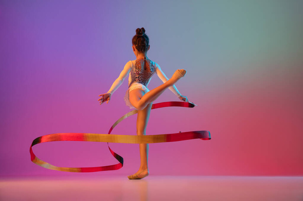 African-american rhythmic gymnast, pretty girl practicing on gradient studio background in neon light - Photo, image