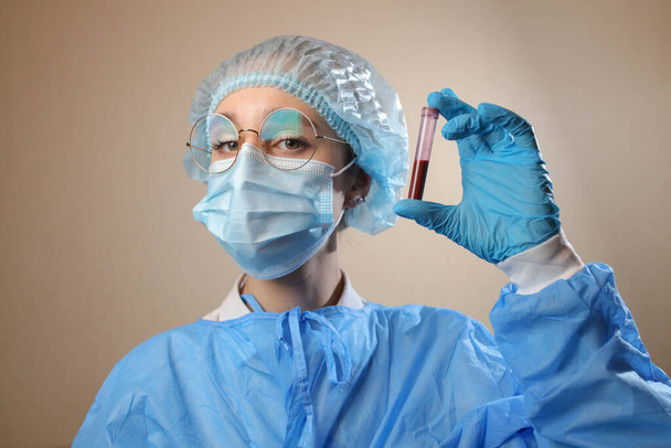 Un médico con una máscara protectora y gafas sostiene en sus manos un tubo de ensayo con una muestra de sangre positiva para el coronavirus. detener el coronavirus. MERS. COVID-19. 2021 pandemia. - Foto, imagen