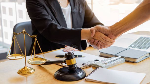 Na een goede samenwerking, een overleg tussen een mannelijke advocaat en een zakenman klant met een hamer en gouden weegschaal op tafel. - Foto, afbeelding
