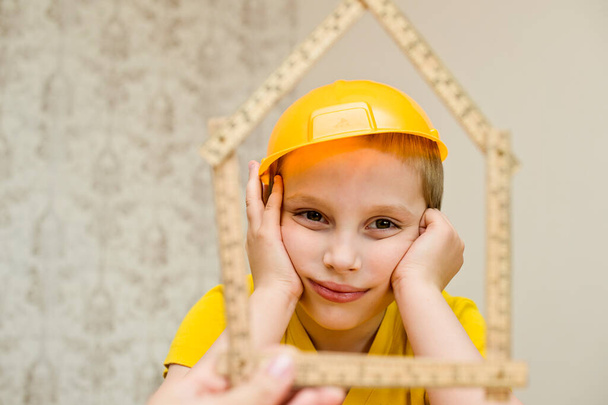 De jonge bouwer. kind met bouwhelm en houten meter in de vorm van huis - Foto, afbeelding