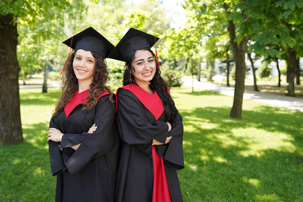 Retrato de estudiantes graduadas exitosas que usan gorra al aire libre cerca de la universidad - Foto, imagen