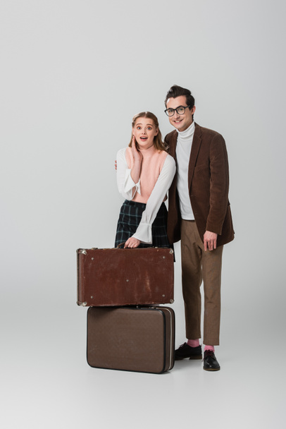 smiling man standing near shocked girlfriend and vintage suitcases on grey background - Foto, immagini