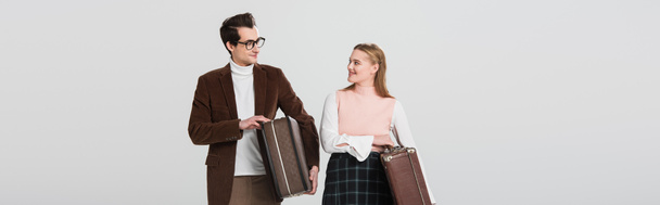 happy couple in vintage outfit looking at each other while holding suitcases isolated on grey, banner - Photo, Image