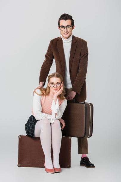 pretty woman sitting on suitcase near man touching her shoulder on grey background - Foto, Imagem