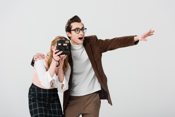 amazed man pointing with hand near girlfriend taking photo on vintage camera isolated on grey - 写真・画像