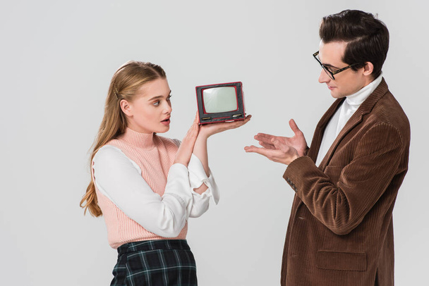 man pointing at vintage tv in hands of surprised woman isolated on grey - Fotografie, Obrázek