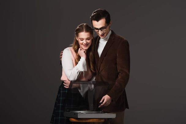 jeune homme étreignant petite amie heureuse tout en se tenant près du tourne-disque vintage isolé sur noir - Photo, image