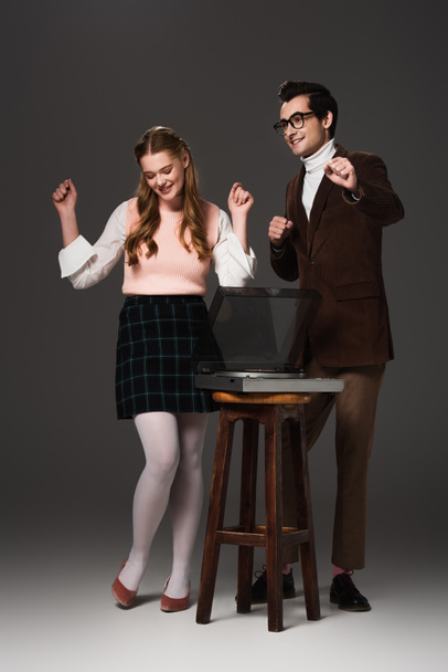 cheerful, old fashioned couple dancing near record player on dark grey background - Foto, Imagem