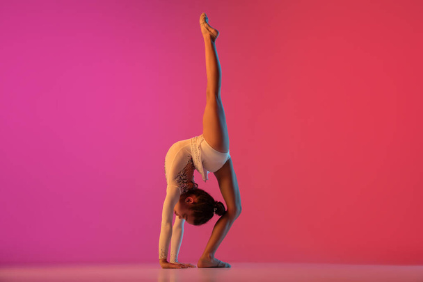 African-american rhythmic gymnast, pretty girl practicing on gradient studio background in neon light - Фото, зображення