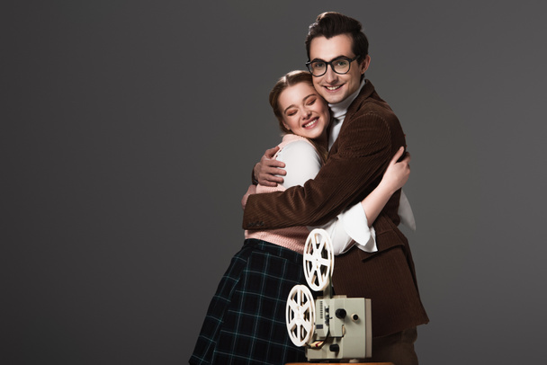 feliz casal à moda antiga abraçando perto projetor de filme isolado em preto - Foto, Imagem