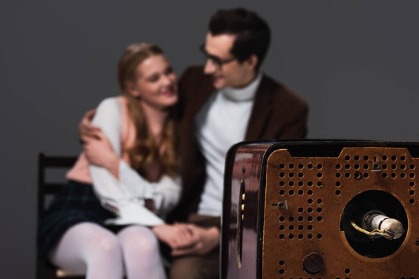 old fashioned couple embracing while watching tv isolated on dark grey, blurred background - Photo, Image