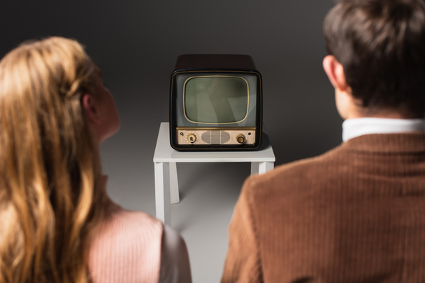 back view of blurred couple watching retro tv on grey background - Zdjęcie, obraz