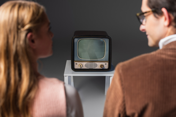 vue arrière du couple flou regardant la télévision vintage sur gris  - Photo, image