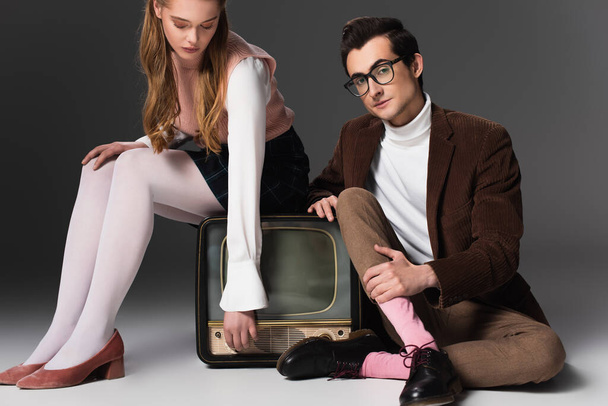 stylish man looking at camera near woman sitting on vintage tv on grey background - Photo, Image