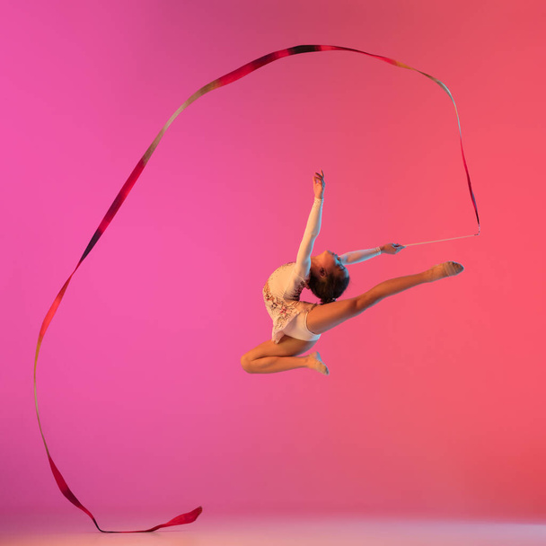 African-american rhythmic gymnast, pretty girl practicing on gradient studio background in neon light - Foto, Imagen
