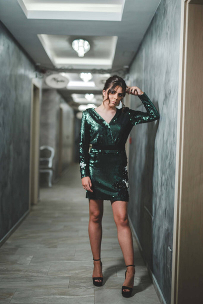 A full body shot of a sexy Bosnian brunette girl in stylish green sequins dress posing in the corridor - Фото, изображение