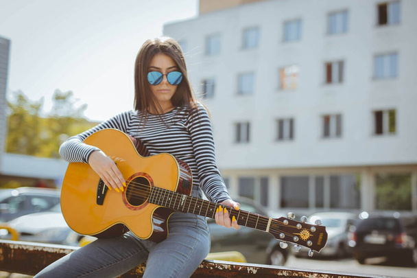 古い道の壁に座っている間にアコースティックギターを演奏する大人の女性の浅い焦点 - 写真・画像