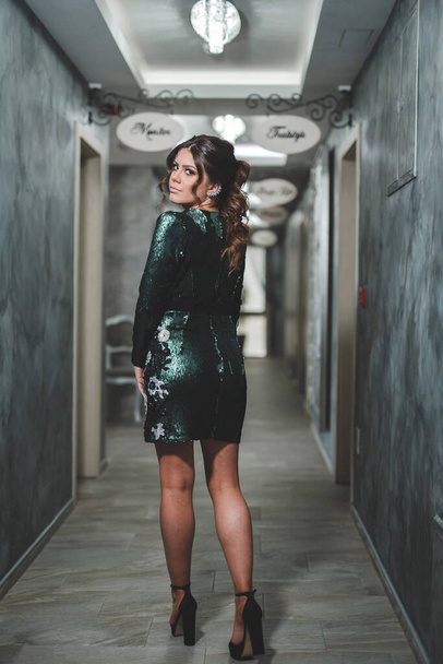 A shallow focus of an adult woman wearing a green sparkling dress with high heels on a restaurant hallway - Photo, image