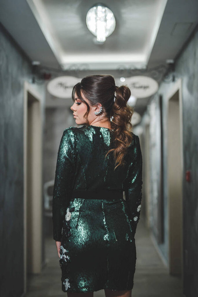 A back view of a sexy Bosnian brunette girl in stylish green sequins dress posing in the corridor - Zdjęcie, obraz