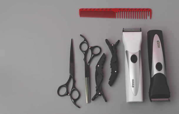 Szakmai Hardressing Tools egy szürke háttér. Olló és vékonyító olló, hajvágó, vörös fésű és hajcsat. Stilizálva klasszikus fekete-fehér színekben fém pengékkel - Fotó, kép