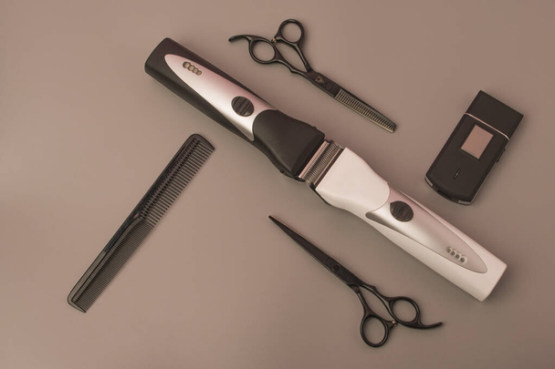 Profesionální hardwarové nástroje na teplém šedém pozadí. Nůžky a tenké nůžky, nůžky na vlasy, holicí strojky a hřeben stylizované v klasické černé a bílé barvě s kovovými čepelemi - Fotografie, Obrázek