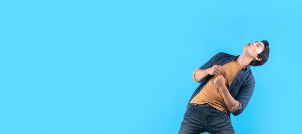 Cheerful Asian male man indicate thumb empty space hand gesture finger point wide smile open mouth wear casual cloth jeans isolated blue color background - 写真・画像