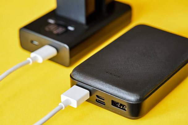 Power bank laadt batterijen op met behulp van een USB-kabel op een gele achtergrond. Close-up, selectieve focus - Foto, afbeelding