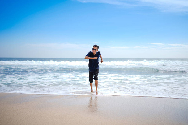 человек в голубой рубашке, преследуемый волнами. этот пляж выглядит красиво, чистый и белый песок. - Фото, изображение