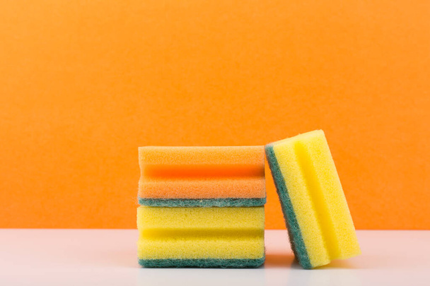 Yellow and orange sponges for house cleaning and dish washing on white table against orange background - Valokuva, kuva