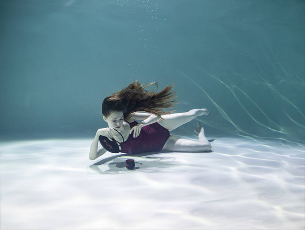 kaunis tyttö punaisessa uimapuvussa värillisellä teekannulla ja kupilla on teekutsut veden alla sinisellä taustalla - Valokuva, kuva