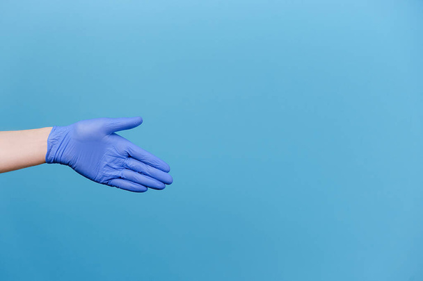 Un gesto de bienvenida. Palma abierta. Primer plano de la mano masculina irreconocible con guantes médicos de protección, aislado sobre fondo azul con espacio de copia para publicidad. Fondo publicitario. Concepto Covid-19 - Foto, imagen