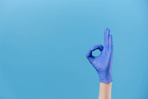Close up of male hand in medical protective gloves demonstrates ok sign, isolated in blue studio background with copy space, expresses celebration and triumph. Body language concept. Gesture concept - Фото, зображення
