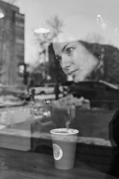 Black and white portrait of a sad woman of 45 years, made through the window of a cafe. - Fotografie, Obrázek