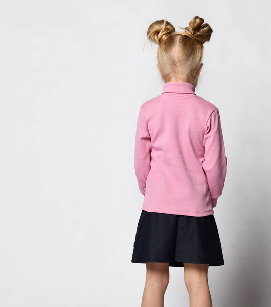 blonde with a stylish hairstyle in a pink turtleneck and a short skirt with daisy flowers, and sneakers posing with her back to the camera on a light background - Photo, image