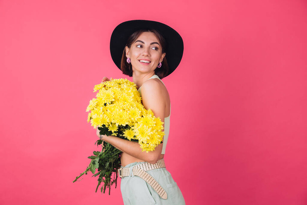 Stylish woman in hat on pink red background hugging large bouquet of yellow asters, spring mood, calm smiling isolated space - 写真・画像