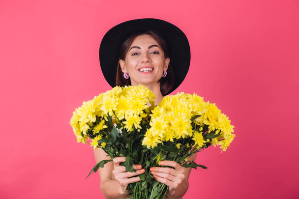 Beautiful stylish woman in hat posing over pink red background holding large bouquet of yellow asters, spring mood, positive emotions isolated space pull to camera - Photo, Image