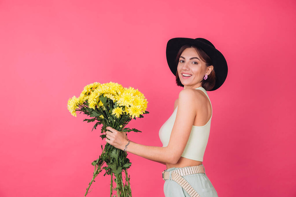 Stylish woman in hat on pink red background sips to left large bouquet of yellow asters, spring mood, happy emotions isolated space - Photo, Image