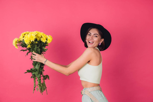 Femme élégante en chapeau sur fond rouge rose sirote à gauche grand bouquet d'asters jaunes, humeur printanière, émotions heureuses espace isolé - Photo, image