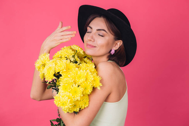 Tyylikäs nainen hattu vaaleanpunainen punainen tausta haju haisee suuri kimppu keltainen asters, kevät mieliala, onnellisia tunteita eristetty tila - Valokuva, kuva