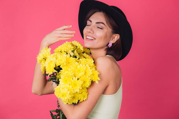 Stylish woman in hat on pink red background smell sniffs large bouquet of yellow asters, spring mood, happy emotions isolated space - Φωτογραφία, εικόνα