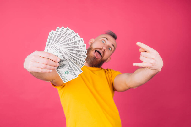 European man on pink red background with fan on 100 dollars with crazy expression rock symbol isolated space - Zdjęcie, obraz